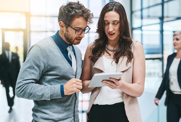 Were going to ace this team task Cropped shot of two young businesspeople working on a digital tablet in a busy office