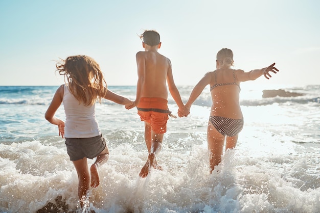 Erano pronti a bagnarsi. inquadratura di fratelli che corrono in acqua sulla spiaggia in una giornata di sole