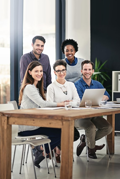 Photo were the team you need full length portrait of a group of businesspeople gathered around a laptop in the office