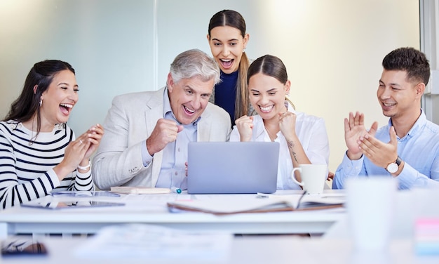 Were on the winning team. Shot of a group of businesspeople cheering while using a laptop at work.