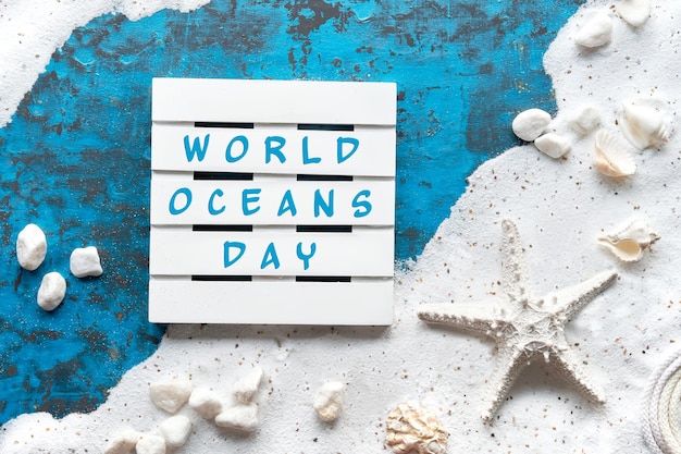 Wereld oceanen dag tekst. Achtergrond met wit zand op turquoise blauwe textuur met schelpen, zeester.