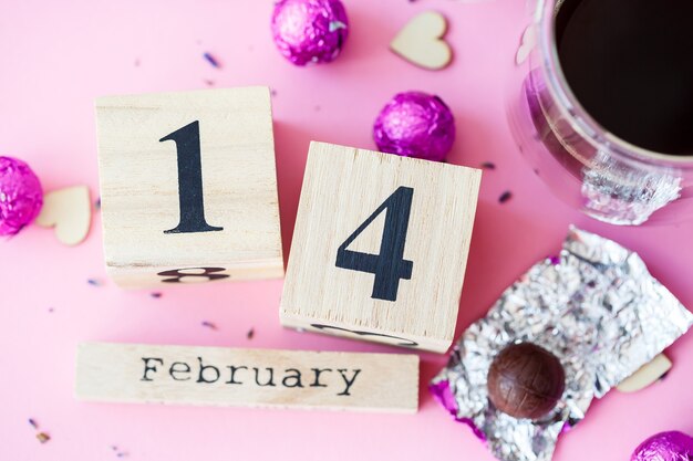 Wereld Valentijnsdag. Houten kalender met datum 14 februari op roze achtergrond met koffie en snoep