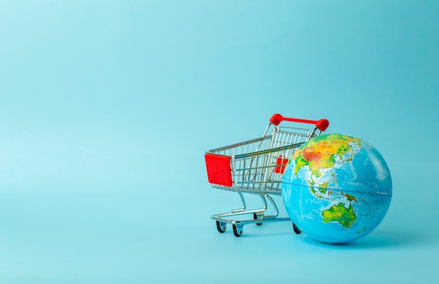 Wereld verkoop en internet verkoop concept. Supermarktkar met aardebol op blauwe achtergrond. Wereldhandel en levering van aankopen
