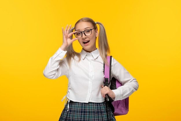 Wereldboekendag blond schoolmeisje met paardenstaarten en roze rugzak die een bril aanraakt