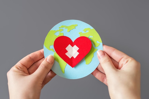 Wereldgezondheidsdag concept Vrouwelijke handen houden een papieren model van de wereld vast met een hart