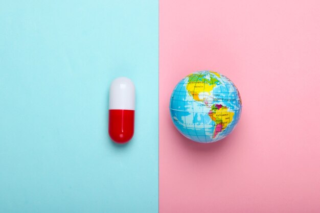 Wereldpandemie. Glopale epidemie. Globe en capsule pil op een blauw-roze pastel muur Bovenaanzicht. Minimalisme