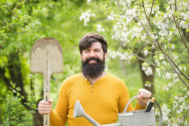 Werk in de tuin, bebaarde man met tuingereedschap, tuinwerk, boerderijwerk in de tuin, lente glimlachende man