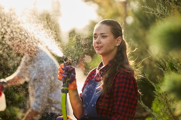 Werk in de tuin. Meisjestuinman spuit water en een man spuit op een zonnige dag kunstmest op planten in de prachtige kwekerij. .