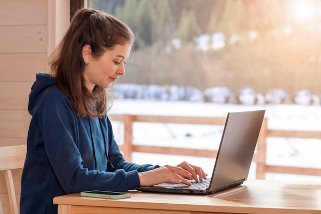 Werk op afstand Freelancer Vrouw werkt op afstand op laptop en telefoon in huisje in winterbergen