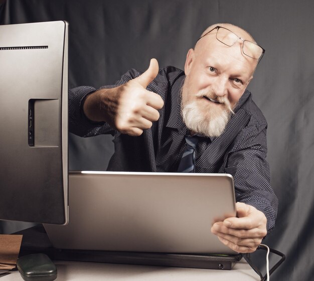 Foto werk op kantoor een vrolijke oudere man met een grijze baard voor een laptop is tevreden met het resultaat