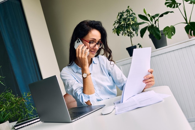 Werk op kantoor Zakenvrouw die aan de telefoon praat terwijl ze documenten vasthoudt