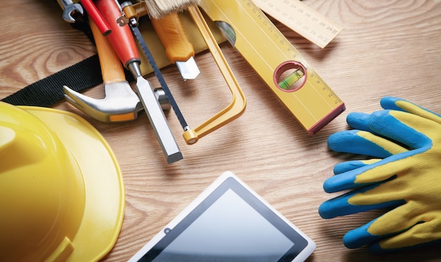 Werk tools met helm, tablet en handschoenen op houten achtergrond.