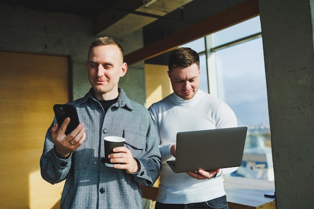 Werk van twee mannelijke collega's die samen op kantoor staan terwijl ze ideeën uitwisselen met een laptop in de vergaderruimte en werkschema's analyseren Werken in een modern, ruim kantoor