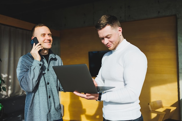 Werk van twee mannelijke collega's die samen op kantoor staan terwijl ze ideeën uitwisselen met een laptop in de vergaderruimte en werkschema's analyseren Werken in een modern, ruim kantoor