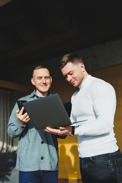 Werk van twee mannelijke collega's die samen op kantoor staan terwijl ze ideeën uitwisselen met een laptop in de vergaderruimte en werkschema's analyseren Werken in een modern, ruim kantoor