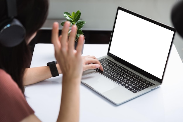 Werk vanuit huis, achterkant van Aziatische jonge zakenvrouw videoconferentiegesprek of facetime-vergadering online op laptopcomputer vooraan hand opsteken om de groep te begroeten quarantaineziekte coronavirus of COVID-19