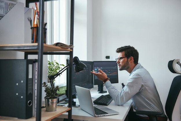 Werkelijk zijaanzicht van verraste jonge mannelijke beursmakelaar die grafieken op computer analyseert