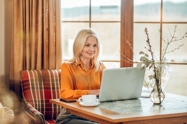 Werken. Blonde langharige vrouw zit aan de tafel en werkt op een laptop