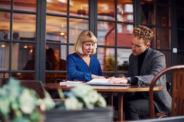 Werken met documenten. Jonge kerel in formele kleding heeft een zakelijk gesprek met oude vrouw in café.