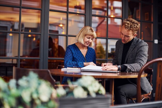 Werken met documenten. Jonge kerel in formele kleding heeft een zakelijk gesprek met oude vrouw in café.