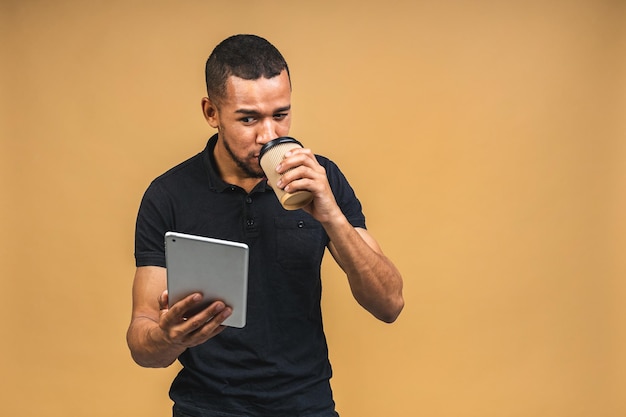 Werken op digitale tablet Portret van gelukkig lachende jonge Afro-Amerikaanse zwarte man met digitale tablet terwijl staande geïsoleerd over beige achtergrond Koffie drinken