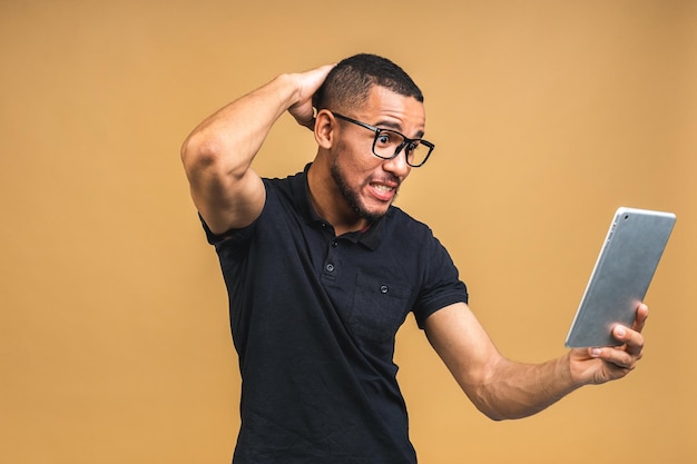Werken op digitale tablet Portret van geschokt verbaasd verrast jonge Afro-Amerikaanse zwarte man met digitale tablet terwijl staande geïsoleerd over beige achtergrond