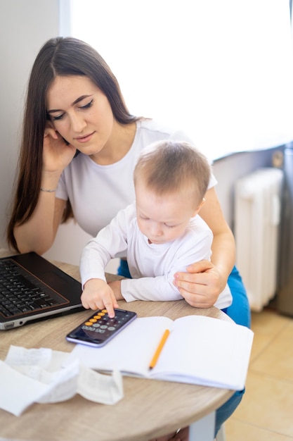 Foto werkend moederconcept jonge vrouw die aan laptop met haar kind van huis werkt