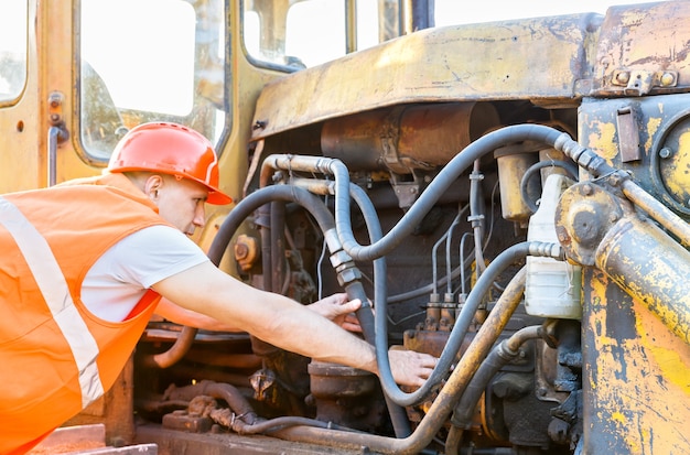 Werkende man in helm bulldozermotor te onderzoeken