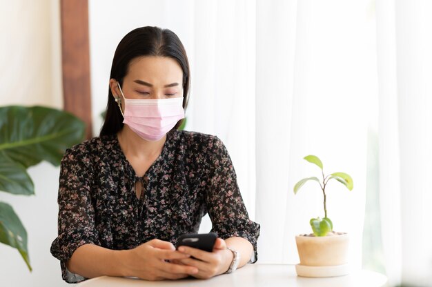 Werkende vrouwen dragen gezichtsmasker met smartphone Thuis zitten werken