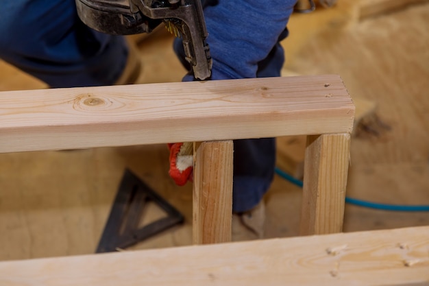 Werklieden die een pneumatisch schiethamer gebruiken, installeren houten framebalken op een nieuw huis in aanbouw