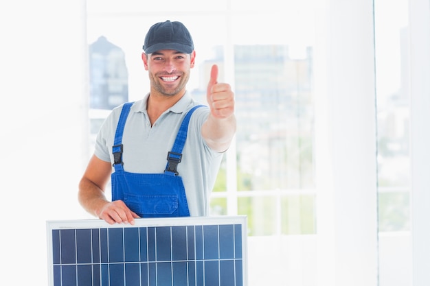 Werkman met zonnepaneel gesturing duimen omhoog in helder bureau