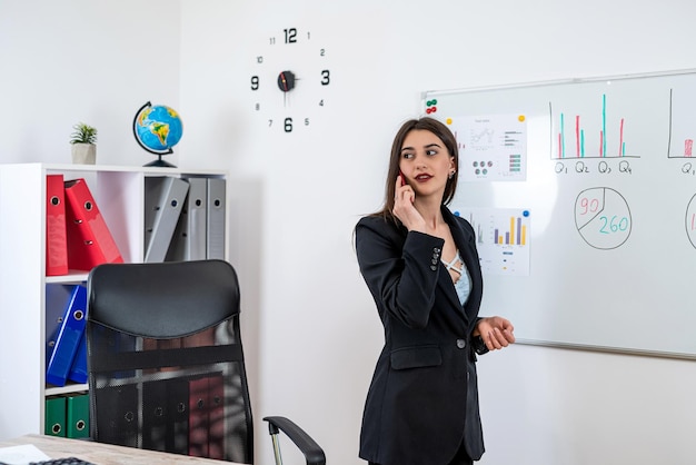 Werkneemster in pak werkt op kantoor in de buurt van flipchart en valt telefonisch