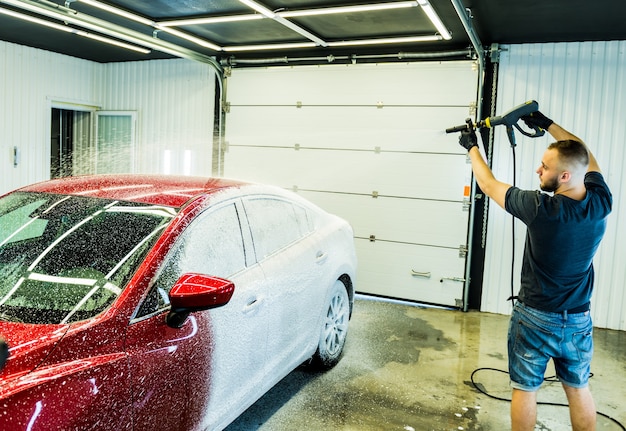 Werknemer auto met actief schuim op een wasstraat wassen.