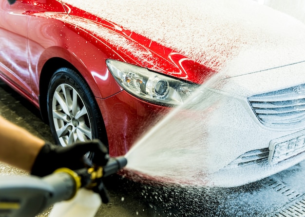 Werknemer auto met actief schuim op een wasstraat wassen.
