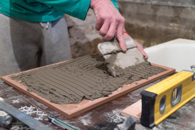 Werknemer brengt cementlijm op de tegels aan. Afwerkingswerken. De technologie van het leggen van tegels