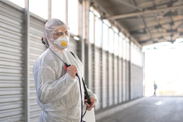 Werknemer die beschermend pak draagt, ontsmettingsuitrusting, desinfecteert de openbare ruimte op het oppervlak