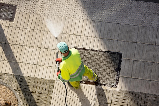 Werknemer die een stoep op straat schoonmaakt met een waterstraalmachine met hoge druk op een zonnige dag Kopieerruimte Bovenbeeld