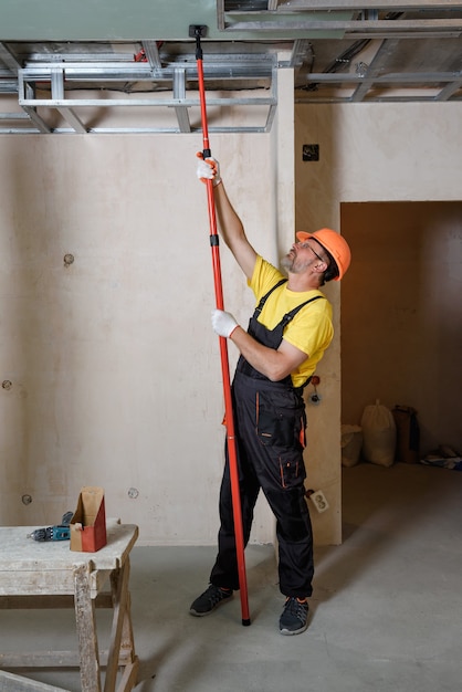 Werknemer die gipsplaat monteert Hij drukt de gipsplaat tegen het plafond