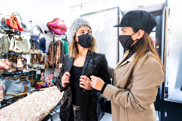 Werknemer en een klant met maskers in een luxe kledingwinkel met een jurk met lovertjes, veiligheidsmaatregelen in de pandemie van het coronavirus, covid-19