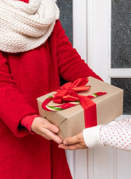 Werknemer gekleed in een rode jas levert geschenkdozen bij de witte deur aan de vooravond van kerstvakantie