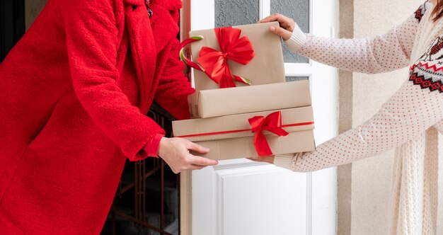 Werknemer gekleed in een rode jas levert geschenkdozen bij de witte deur aan de vooravond van kerstvakantie