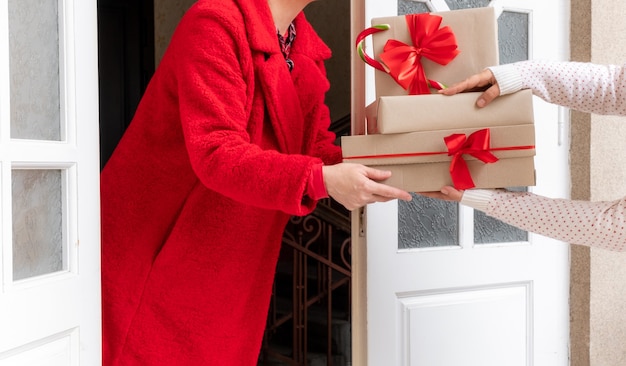 Werknemer gekleed in een rode jas levert geschenkdozen in de buurt van de witte deur aan de vooravond van vakantie Kerstmis en Nieuwjaar.