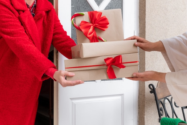 Werknemer gekleed in een rode jas levert geschenkdozen in de buurt van de witte deur aan de vooravond van vakantie Kerstmis en Nieuwjaar.