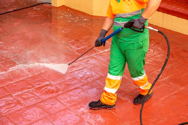 Werknemer gekleed in groene werkkleding, maakt de straten schoon ter voorkoming van covid19 of crown virus met een bleekwaterpistool onder druk