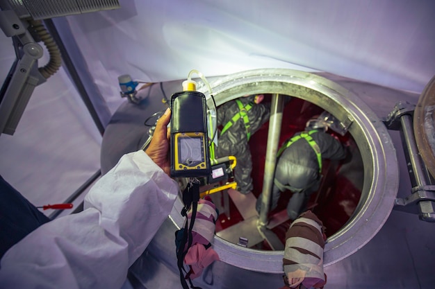 Foto werknemer hand met gasdetector inspectie veiligheidsgas testen aan voorzijde mangat roestvrij tank om binnen beperkt te werken
