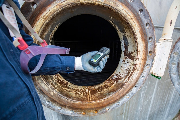 Werknemer hand met gasdetector inspectie veiligheidsgas testen aan voorzijde mangat roestvrij tank om binnen beperkt te werken