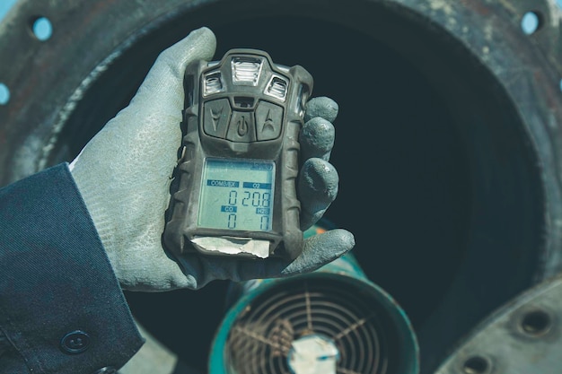 Werknemer hand met gasdetector inspectie veiligheidsgas testen bij voorste mangattank