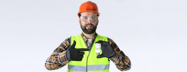 Werknemer in een helm en beschermende kleding met een gloeilamp in zijn handen