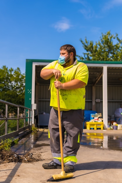 Werknemer in een recyclingfabriek of schoon punt en vuilnis met een gezichtsmasker en met beveiligingsmaatregelen. portret werknemer met een bezem