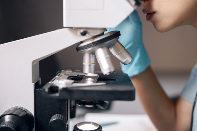 Werknemer in handschoenen kijkt naar monster door microscoop op werkplek in laboratorium